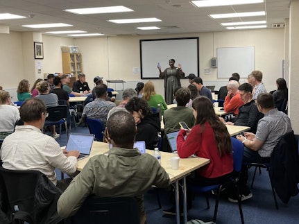 A group of Next Gen Forum members sit around tables listening to a speaker