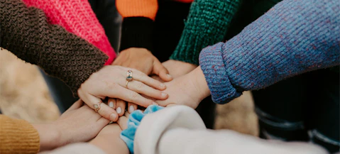 A group of people clasping hands with shared mission, together.