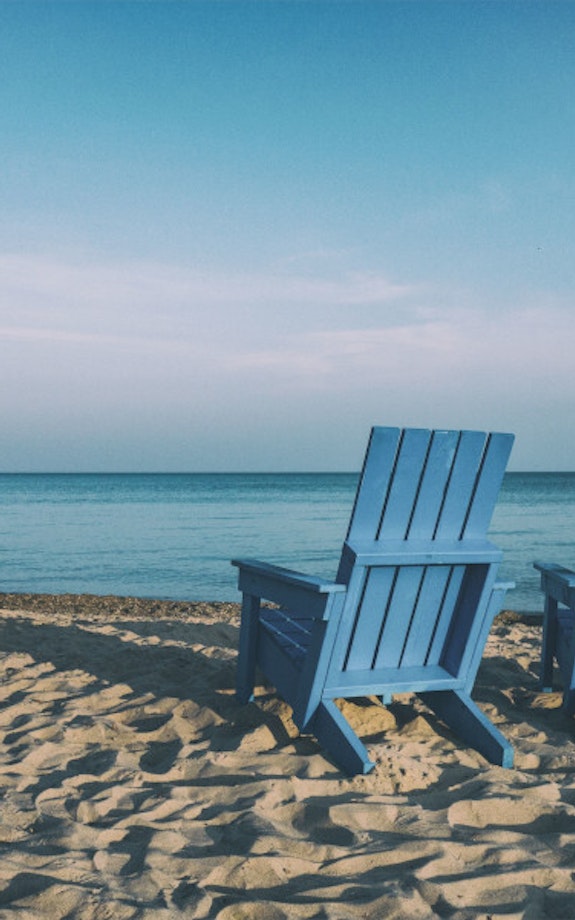 Two blue deck chairs on the beach facing the sea, waiting for a pension scheme recipient