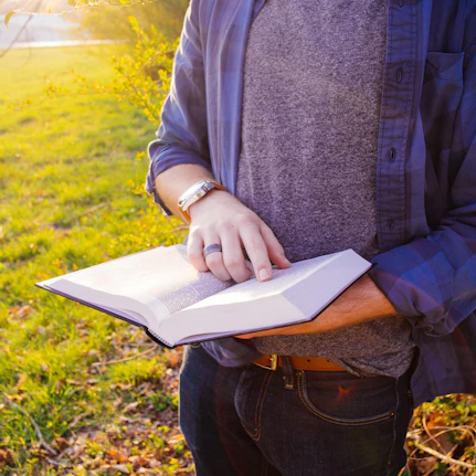 A person stands by a tree reading the bible.