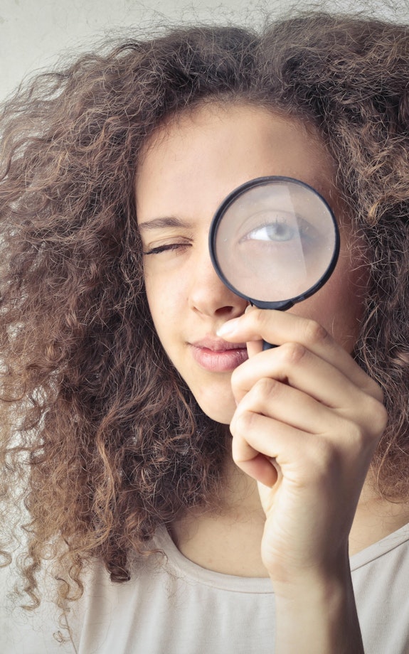 A woman looks at the camera through a magnifying glass